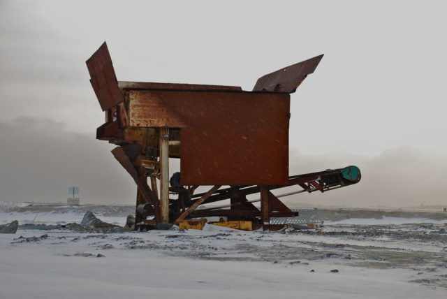 traditional conferences are obsolete: photograph of a large abandoned machine housed in an open building in the middle of a snowy plain. It has brown metal sides and a slanted conveyer belt that extends outside the building.