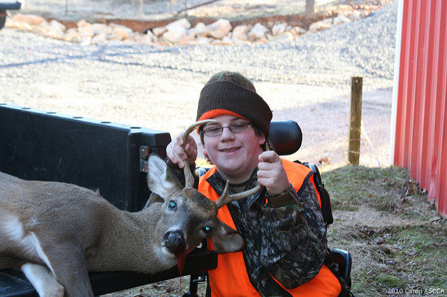 Photograph of a child holding the antlers of a dead buck lying in the back of a pickup truck. Photo attribution: Flickr user campascca.