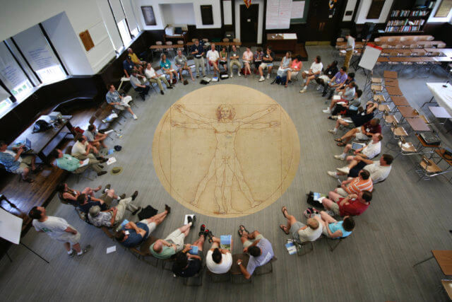 squaring the circle: An overhead photograph of a group of people sitting in a large circle with Leonardo de Vinci's "Vitruvian Man" superimposed at the center